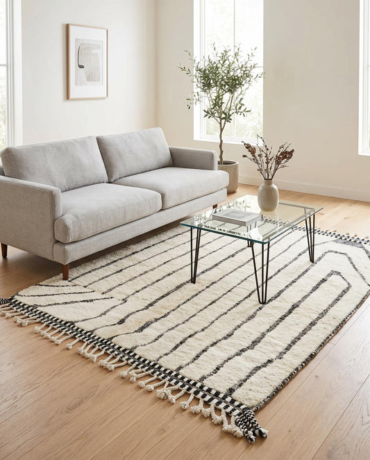 A plush cream and black abstract Moroccan rug by NURA styled in a modern living room with a woven leather chair.