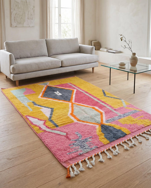 Colorful abstract Moroccan rug in mustard and pink styled in a bright minimalist living room with a woven leather chair by NURA.