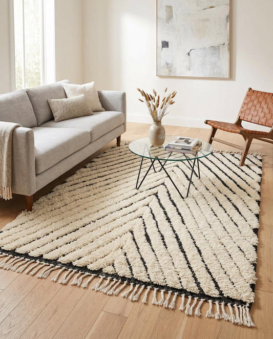 A modern cream and black chevron Moroccan rug by NURA, styled in a minimalist living room with a woven leather accent chair.