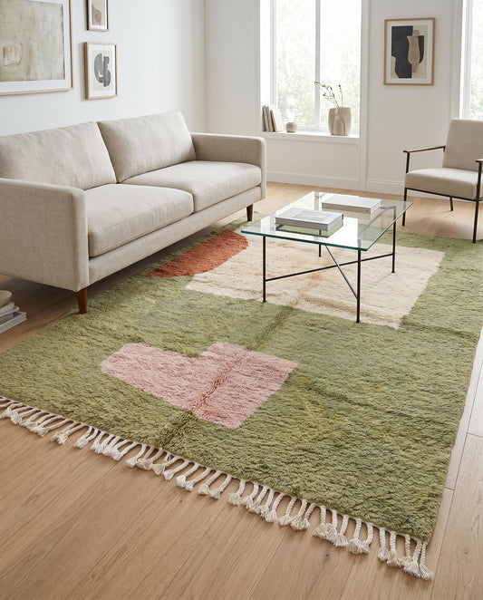 A modern living room styled with a plush sage green Moroccan rug featuring abstract cream, rust, and blush color blocks by NURA.
