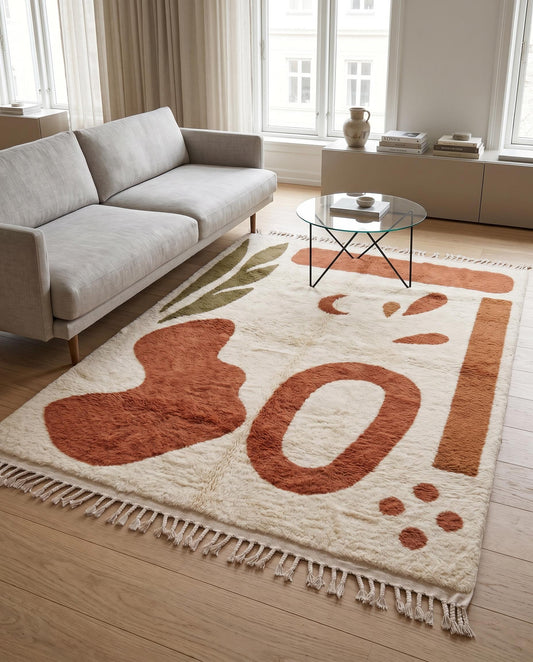 A plush cream Moroccan rug with terracotta and olive abstract shapes styled in a warm, contemporary living room setting by NURA.