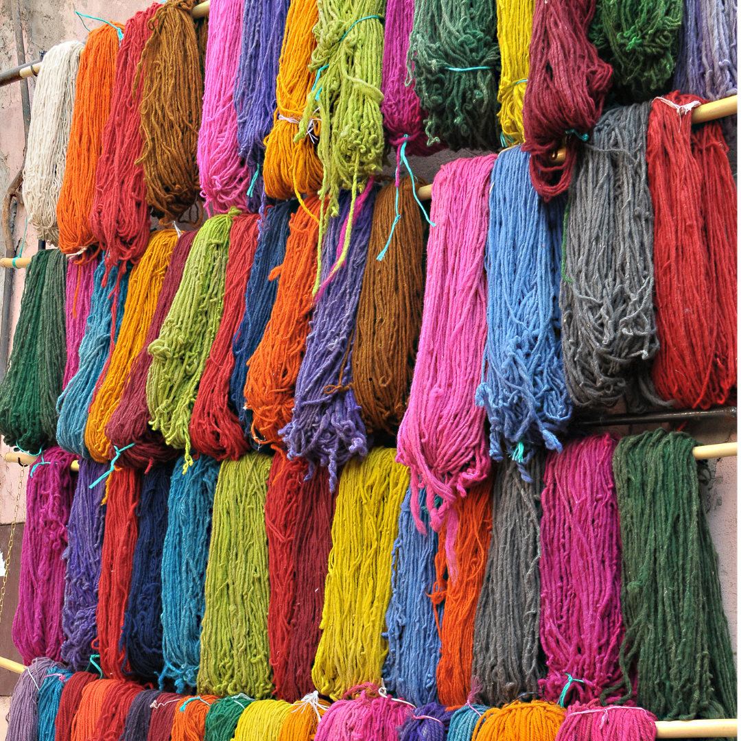 Colorful wool yarn skeins hanging on wooden rods, showing the dyed fibers used to handweave NURA Moroccan rugs.