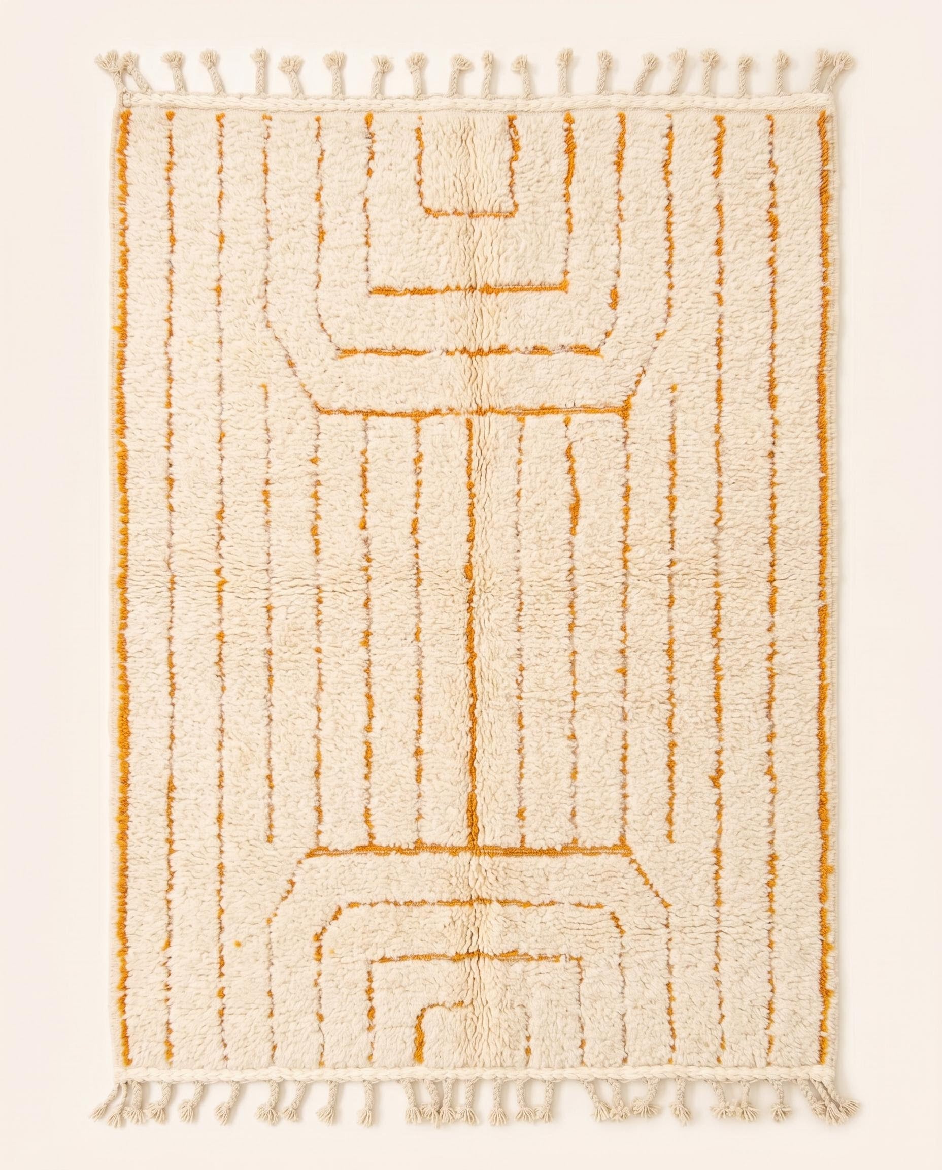 A plush cream Moroccan rug featuring minimalist saffron geometric lines and braided fringe, hand-knotted from wool by NURA.