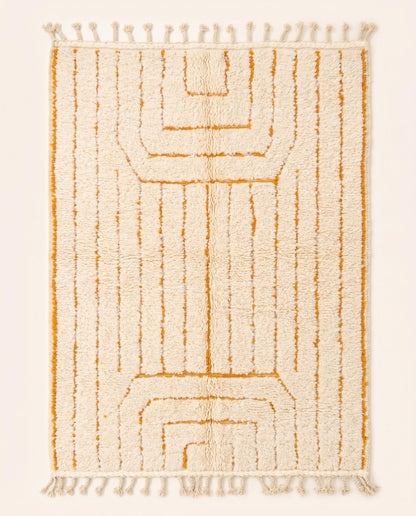 A plush cream Moroccan rug featuring minimalist saffron geometric lines and braided fringe, hand-knotted from wool by NURA.