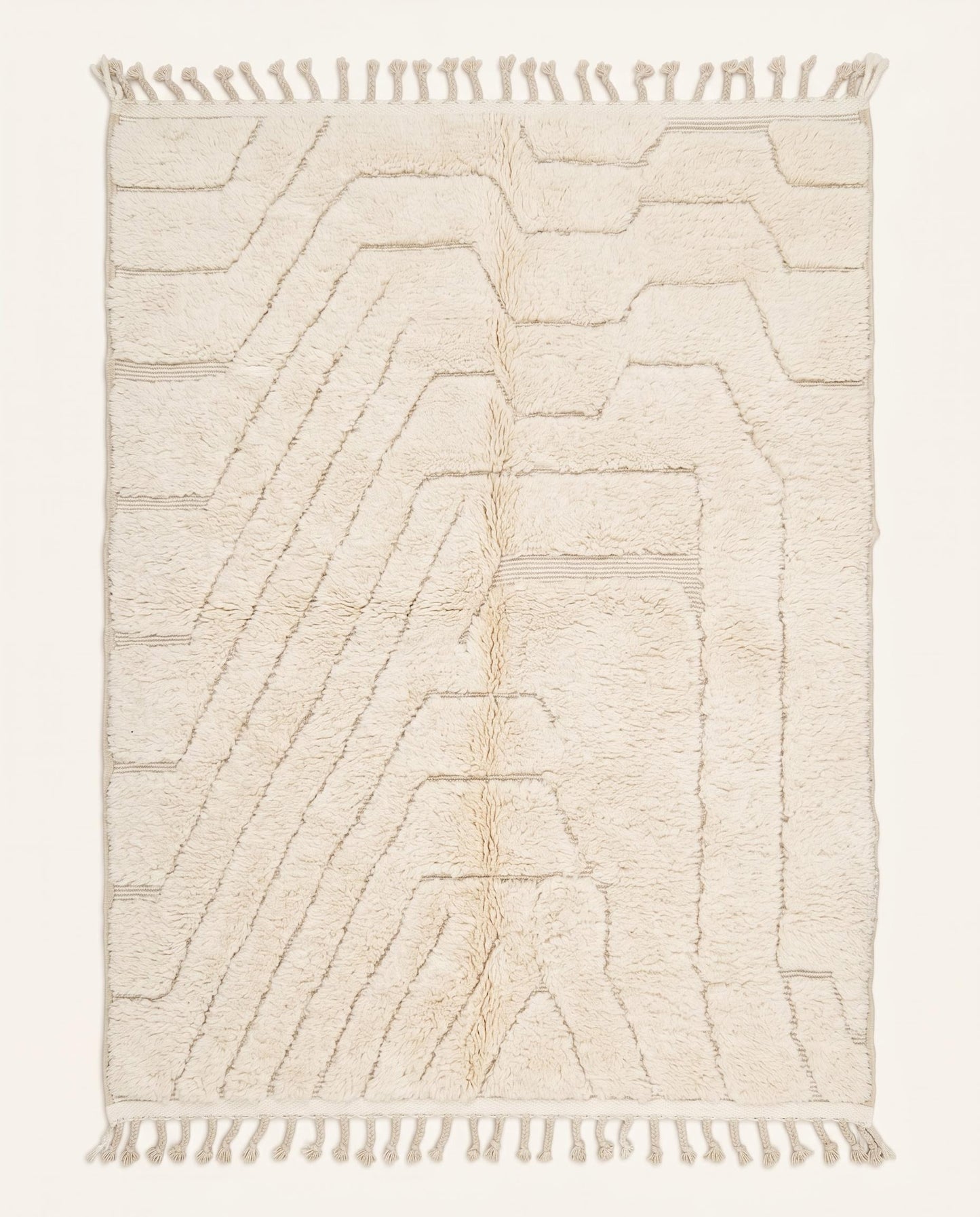 A minimalist Beni Ourain Moroccan rug by NURA featuring a plush cream wool pile with carved geometric lines and braided tassels.