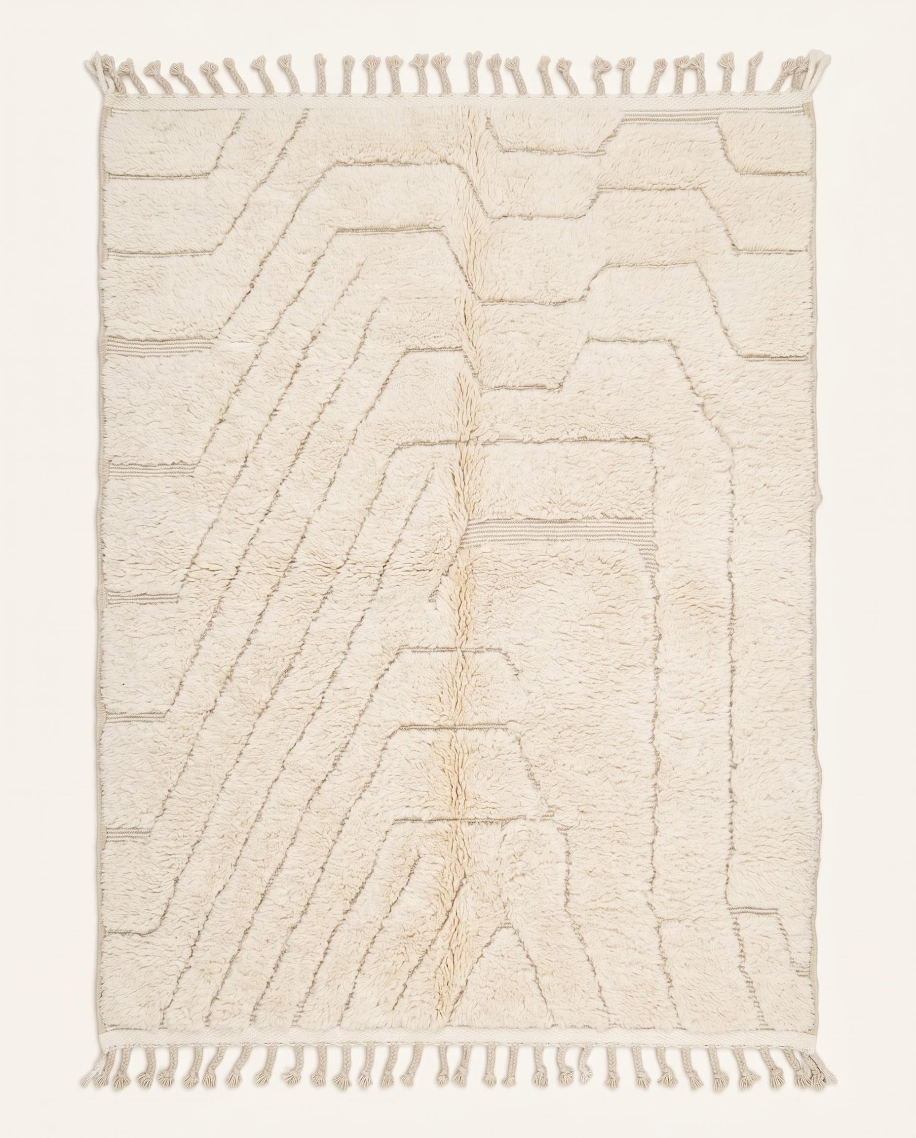 A minimalist Beni Ourain Moroccan rug by NURA featuring a plush cream wool pile with carved geometric lines and braided tassels.
