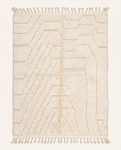 A minimalist Beni Ourain Moroccan rug by NURA featuring a plush cream wool pile with carved geometric lines and braided tassels.