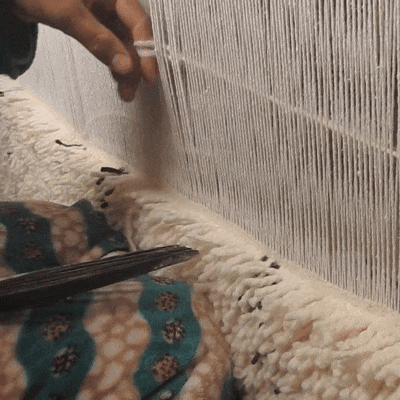 Close-up of an artisan tying hand knots on a Moroccan wool rug loom, showing the traditional handmade process behind NURA rugs.