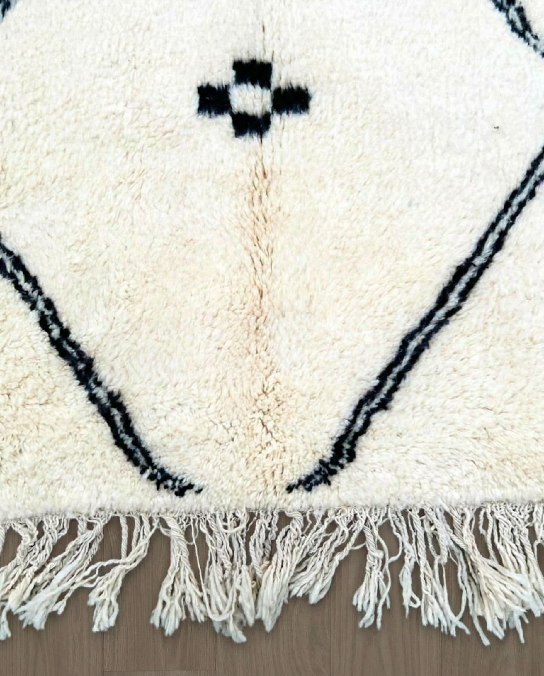 ASMA Beni Ourain cream central double diamond Moroccan rug close-up of hand-tied fringe and kilim band detail, by NURA