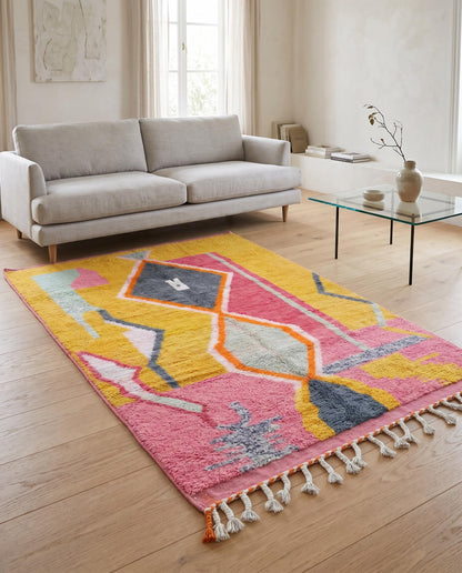 Colorful abstract Moroccan rug in mustard and pink styled in a bright minimalist living room with a woven leather chair by NURA.