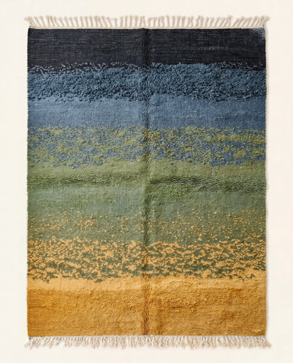 A contemporary Moroccan rug featuring an abstract landscape design with horizontal ombré bands of mustard, sage, denim, and black.