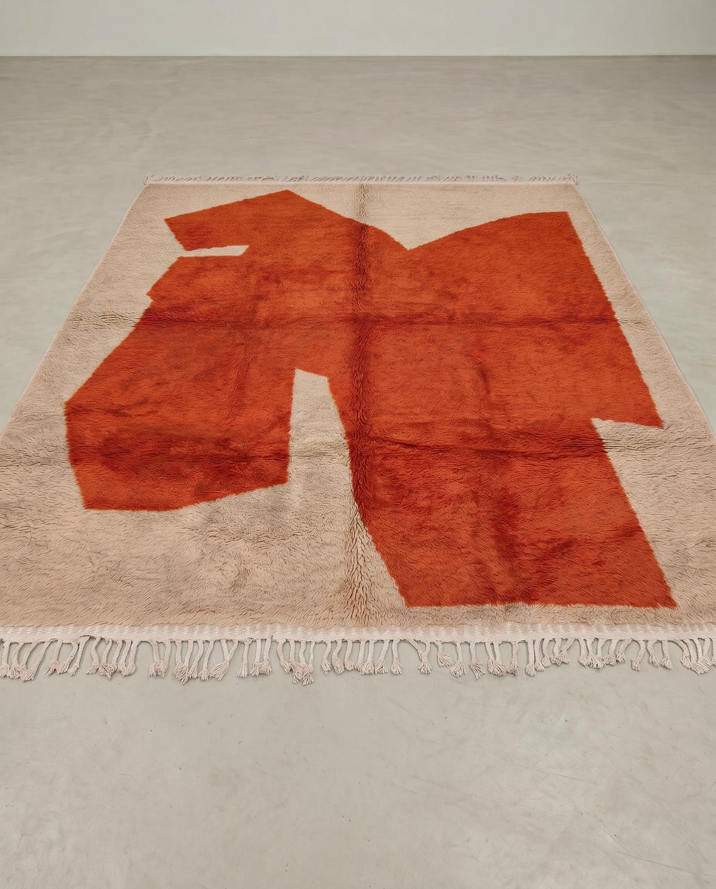 DIMA Beni Ourain rust abstract color block Moroccan rug displayed on a parquet wood floor, showing full fringe and edge detail, by NURA