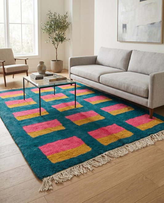 A colorful Moroccan wool rug with a teal, pink, and mustard geometric grid styled in a bright contemporary living room by NURA.