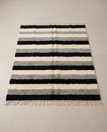 HANIYA Beni Ourain black color block Moroccan rug displayed on a parquet wood floor, showing full fringe and edge detail, by NURA