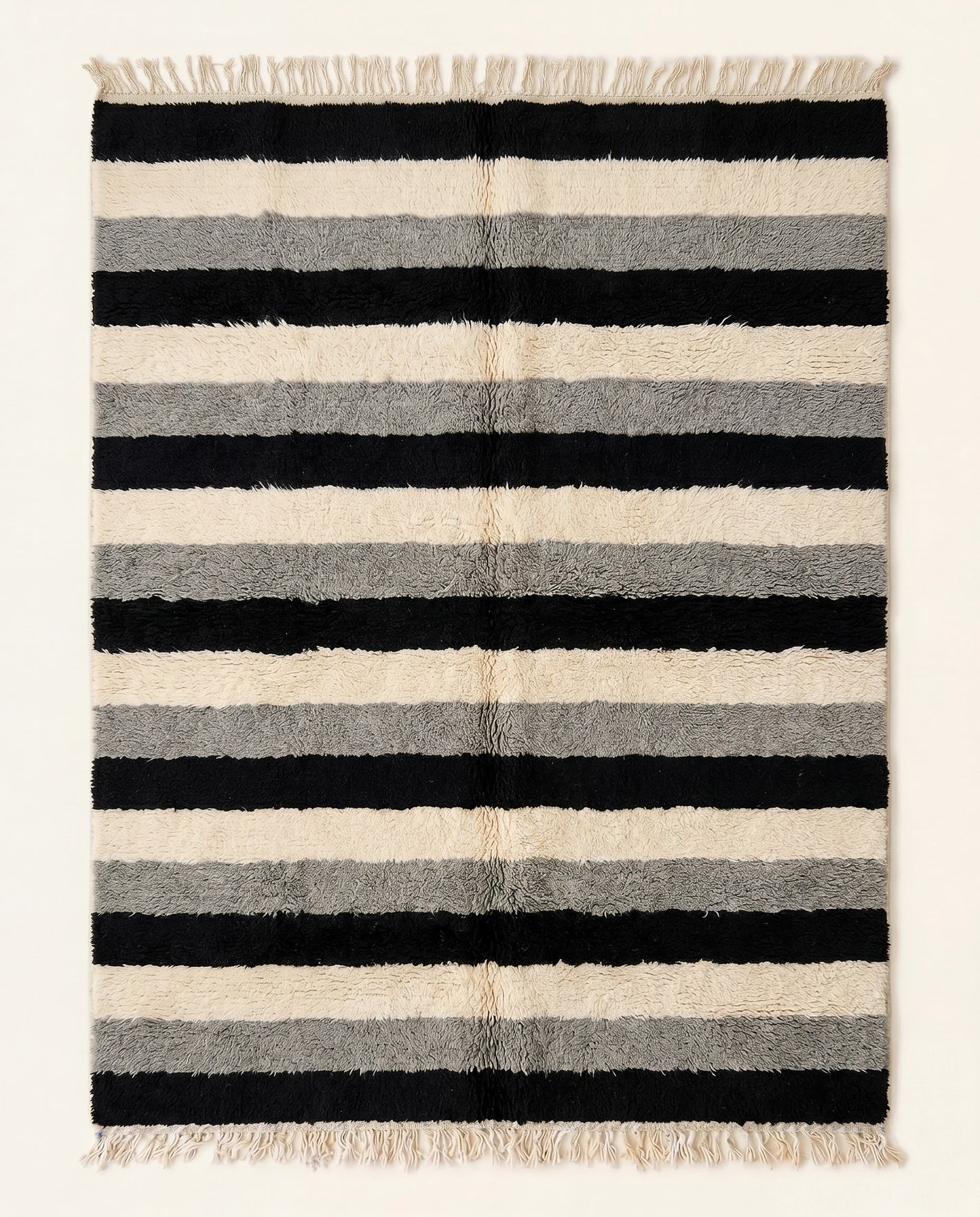 A plush Moroccan wool rug featuring thick horizontal stripes in bold black, cream, and grey, hand-knotted by NURA.