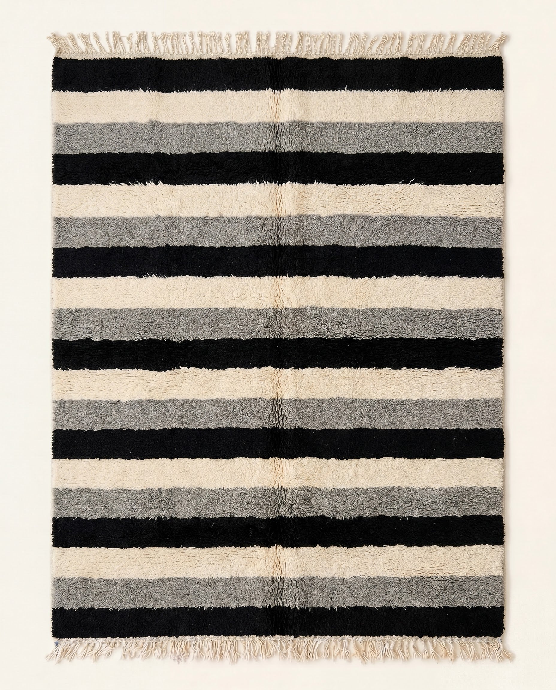 A plush Moroccan wool rug featuring thick horizontal stripes in bold black, cream, and grey, hand-knotted by NURA.