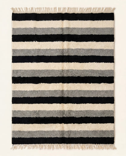 A plush Moroccan wool rug featuring thick horizontal stripes in bold black, cream, and grey, hand-knotted by NURA.