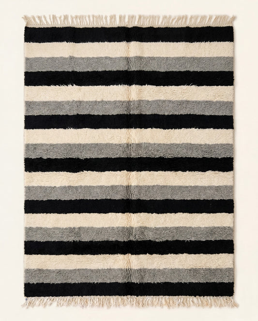 A plush Moroccan wool rug featuring thick horizontal stripes in bold black, cream, and grey, hand-knotted by NURA.