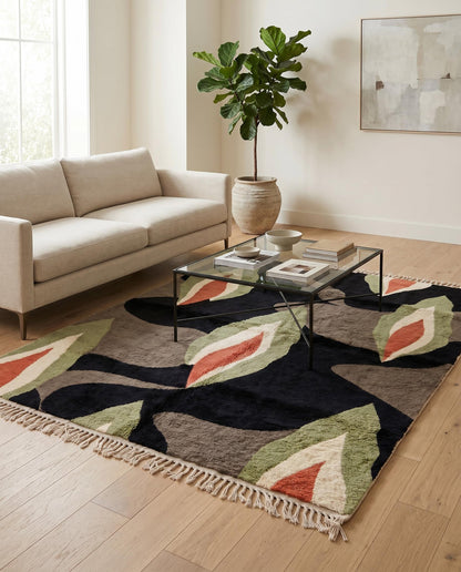 An abstract Moroccan wool rug styled in a modern living room with a grey sofa, glass coffee table, and white chair by NURA.