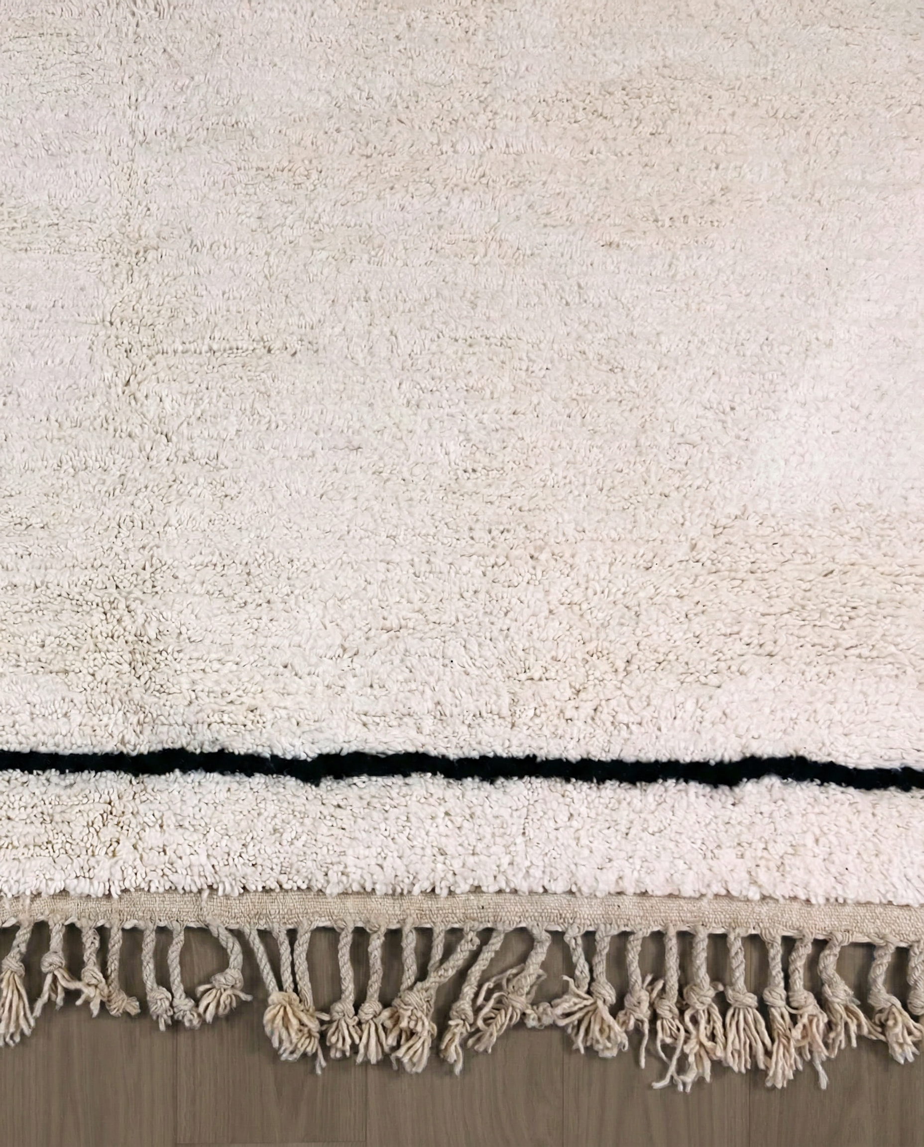 IKRAM Beni Ourain ivory solid border Moroccan rug close-up of hand-tied fringe and kilim band detail, by NURA