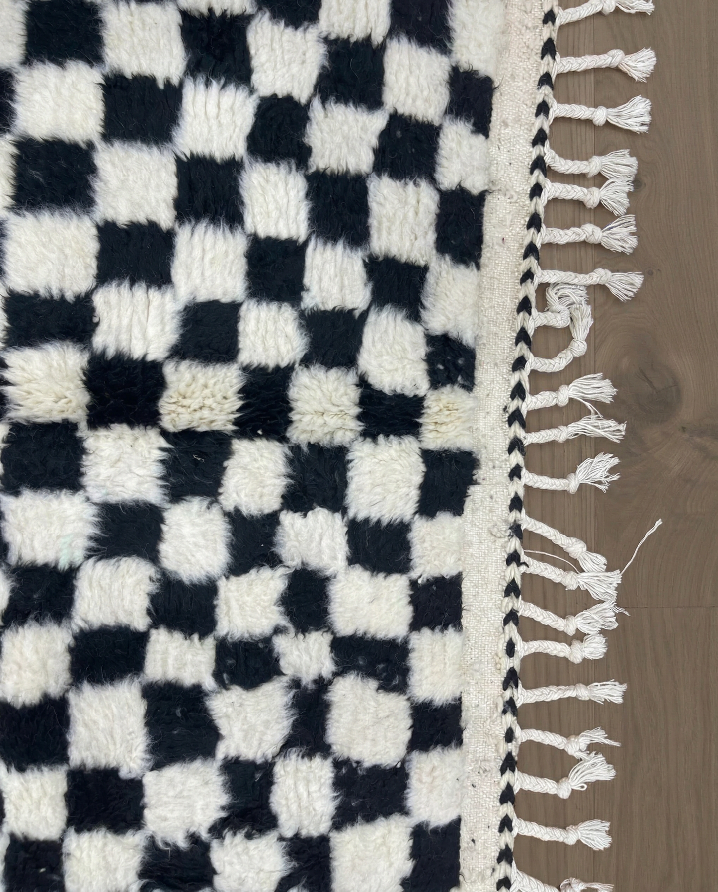 JAMILA Beni Ourain black checker grid Moroccan rug close-up of hand-tied fringe and kilim band detail, by NURA