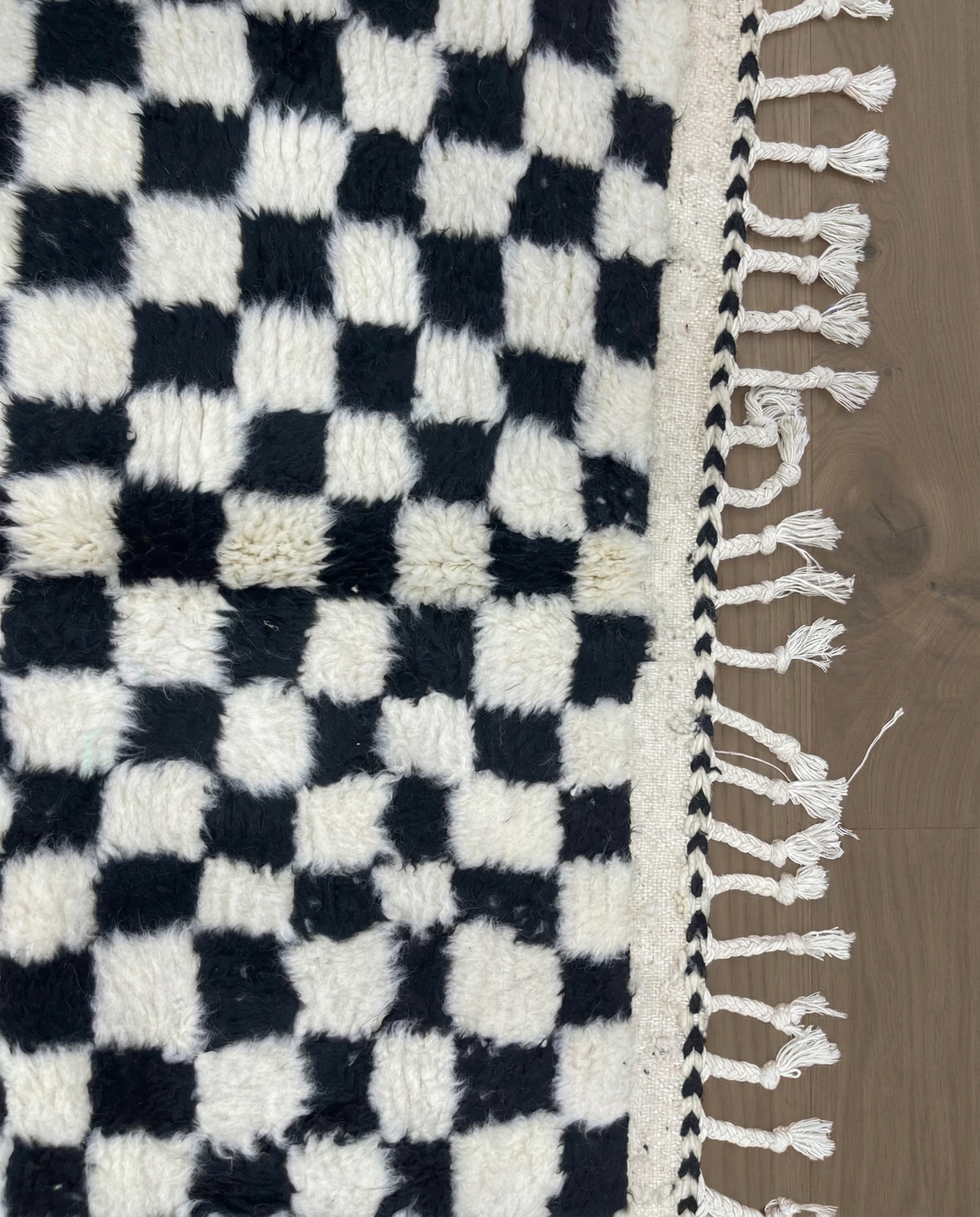 JAMILA Beni Ourain black checker grid Moroccan rug close-up of hand-tied fringe and kilim band detail, by NURA