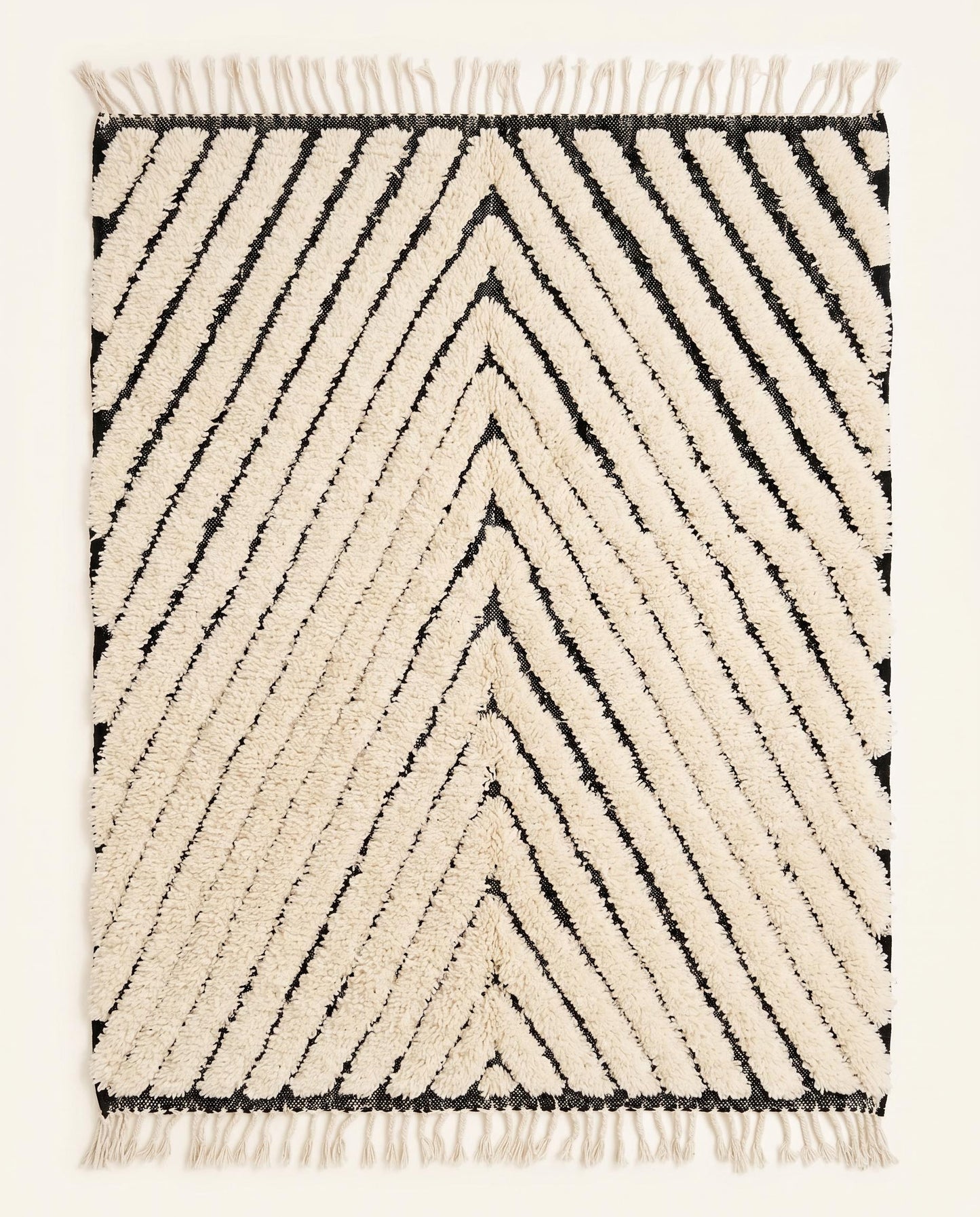 A plush cream Moroccan rug featuring bold black chevron lines and a thick wool pile, shown flat against a white wall by NURA.