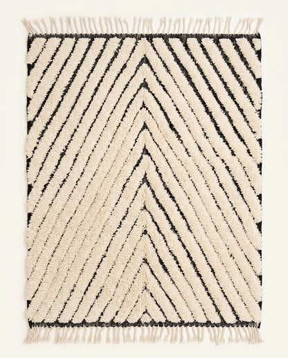 A plush cream Moroccan rug featuring bold black chevron lines and a thick wool pile, shown flat against a white wall by NURA.