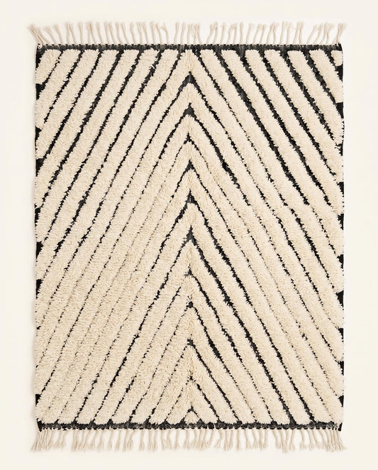 A plush cream Moroccan rug featuring bold black chevron lines and a thick wool pile, shown flat against a white wall by NURA.
