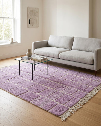 A modern purple Moroccan rug with a cream checker grid pattern styled in a bright living room with a leather chair by NURA.