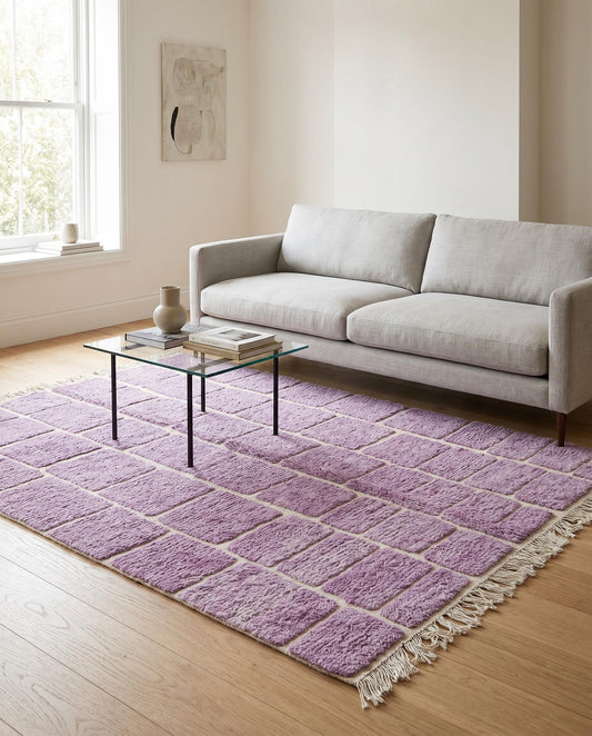 A modern purple Moroccan rug with a cream checker grid pattern styled in a bright living room with a leather chair by NURA.