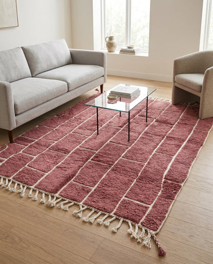 A dusty rose Moroccan rug with an irregular cream block grid, styled in a modern living room setting by NURA.