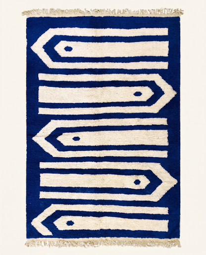 Plush ivory Beni Ourain Moroccan rug with bold cobalt blue graphic arrow bands and a high pile, by NURA.