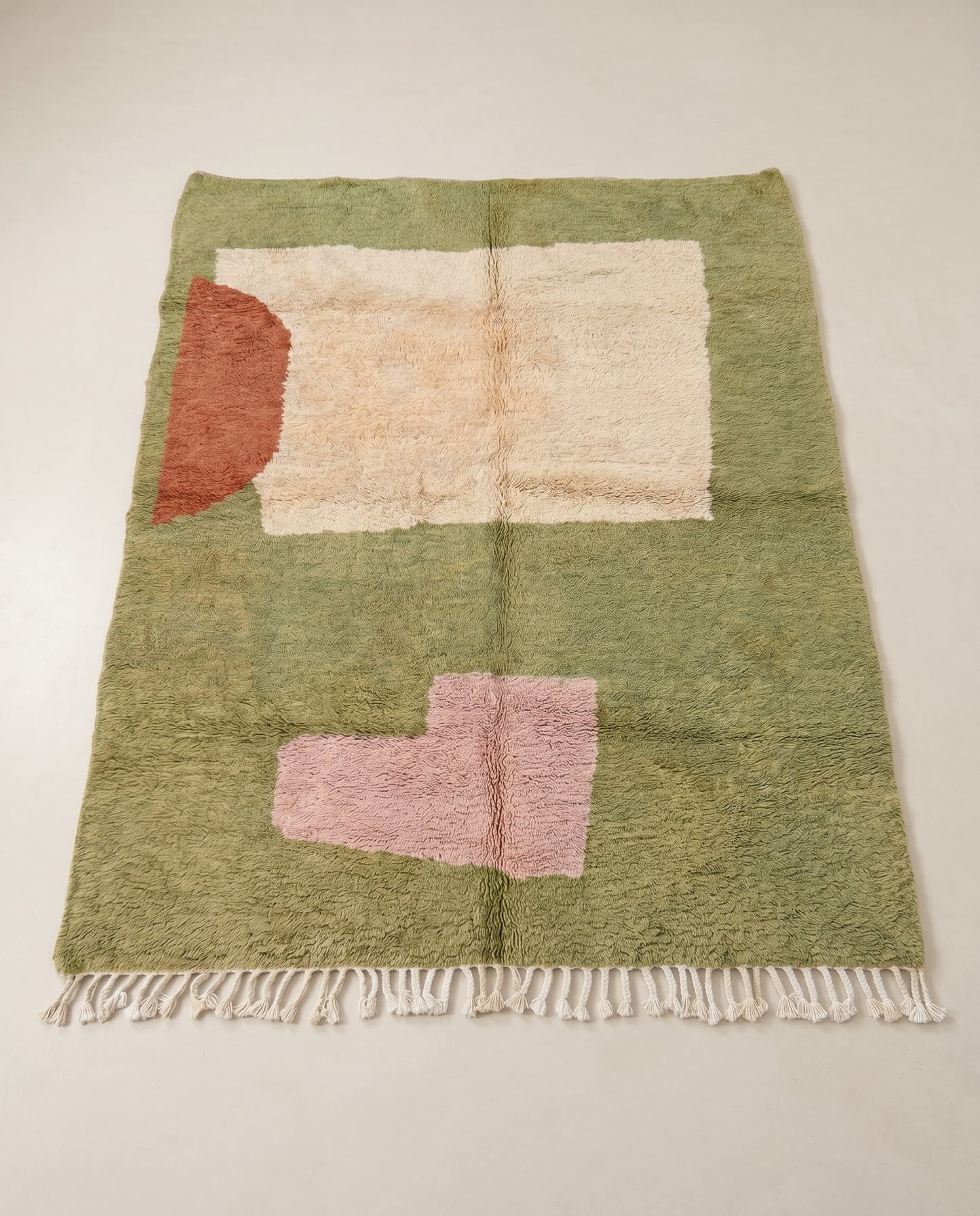 SOULEF Azilal sage color block Moroccan rug displayed on a parquet wood floor, showing full fringe and edge detail, by NURA