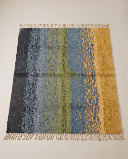 WISSAL Mrirt slate blue organic abstract Moroccan rug displayed on a parquet wood floor, showing full fringe and edge detail, by NURA