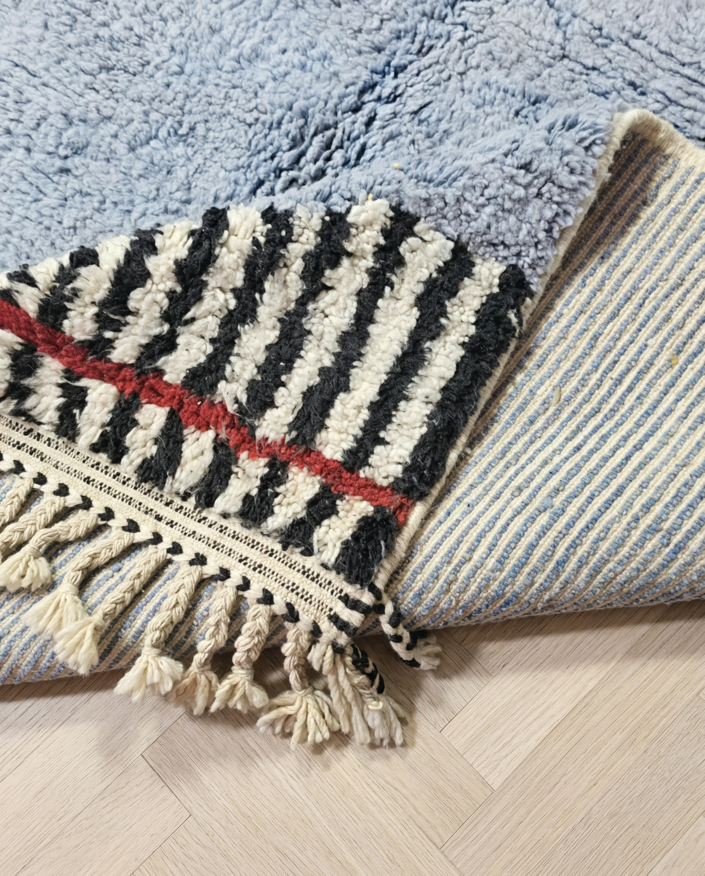 YASMINE Azilal powder blue asymmetrical striped border Moroccan rug close-up of hand-tied fringe and kilim band detail, by NURA
