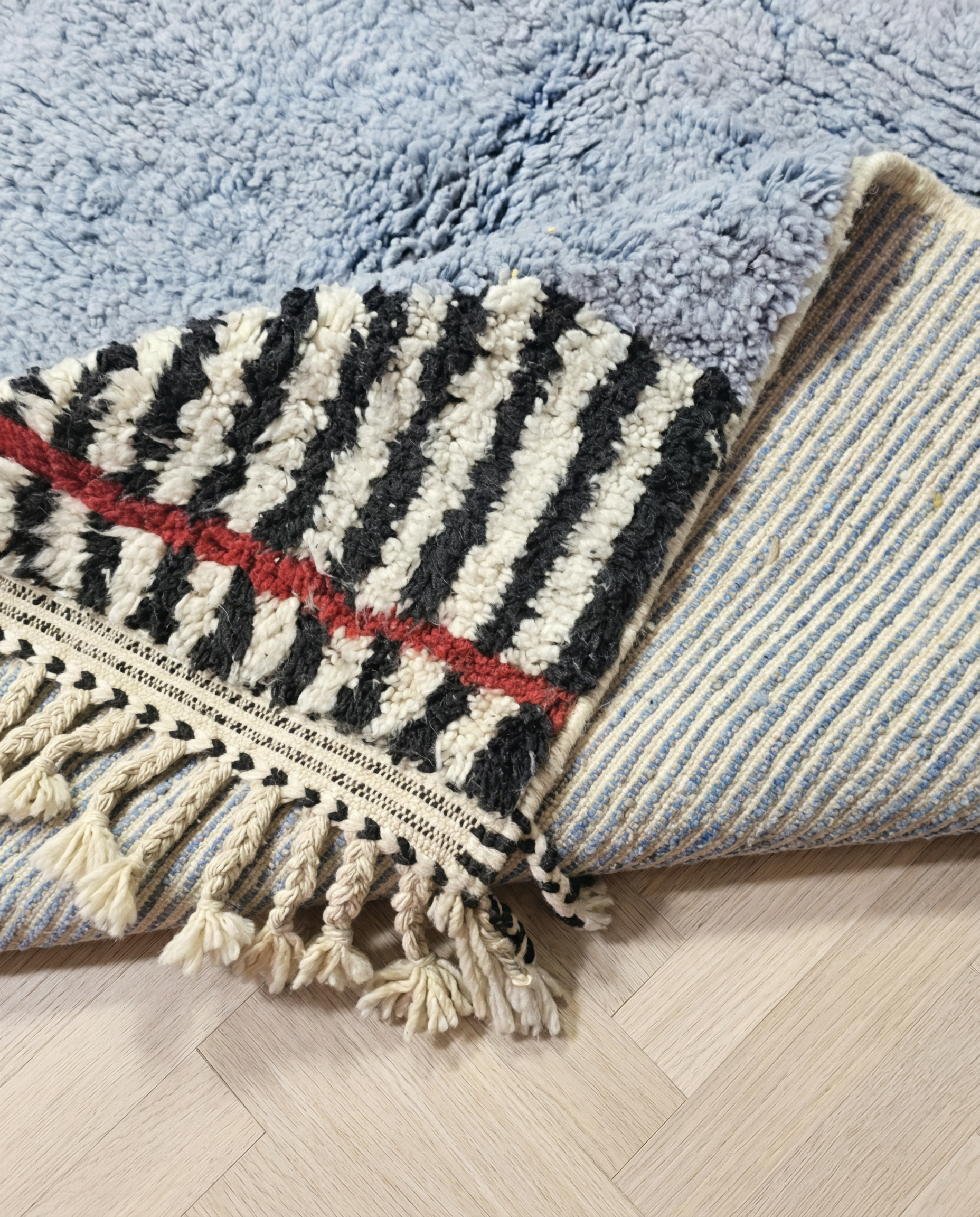 YASMINE Azilal powder blue asymmetrical striped border Moroccan rug close-up of hand-tied fringe and kilim band detail, by NURA