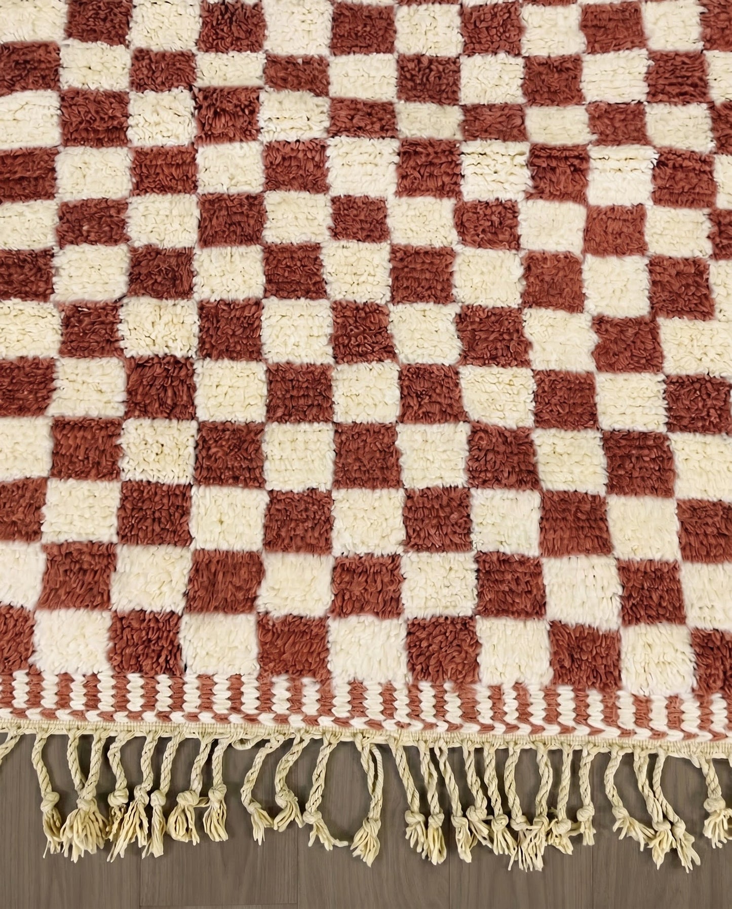ZAHIA Beni Ourain terracotta checker grid Moroccan rug close-up of hand-tied fringe and kilim band detail, by NURA