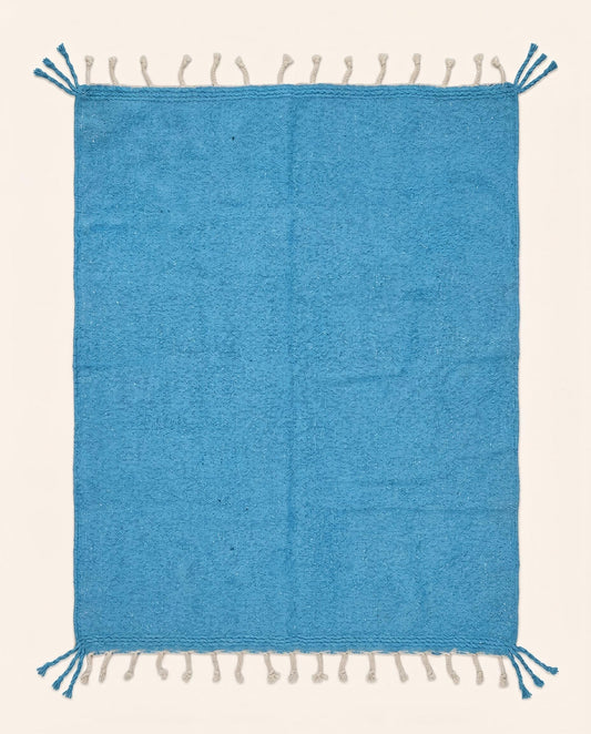 A vibrant solid azure blue Moroccan flatweave rug handwoven from natural wool, featuring braided fringes by NURA.