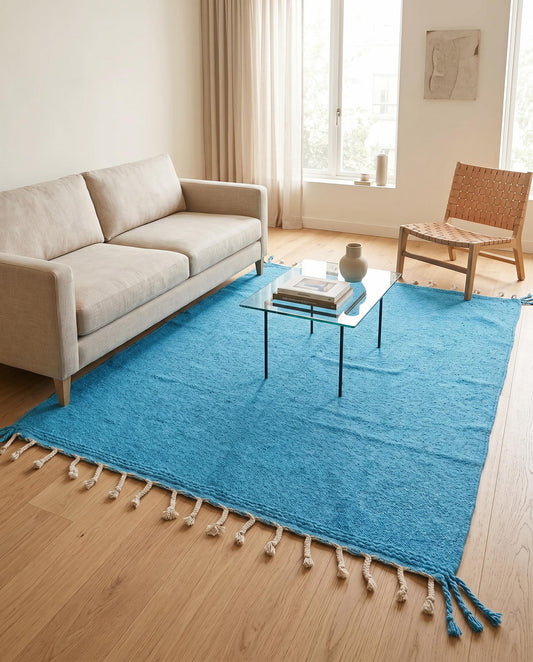 The solid azure blue Moroccan flatweave rug styled in a bright, modern living room with minimalist wooden furniture.